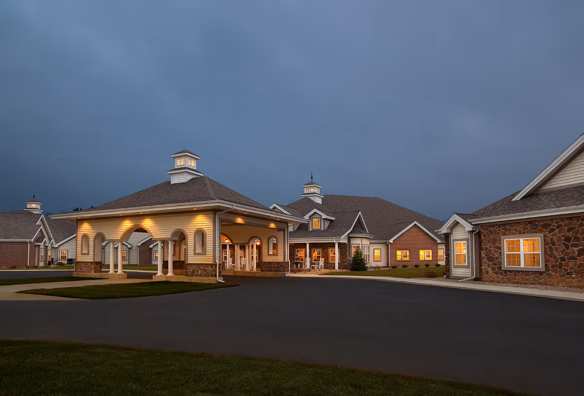 Well-lit senior living facility entrance with a covered porte-cochère and connected single-story buildings at dusk.