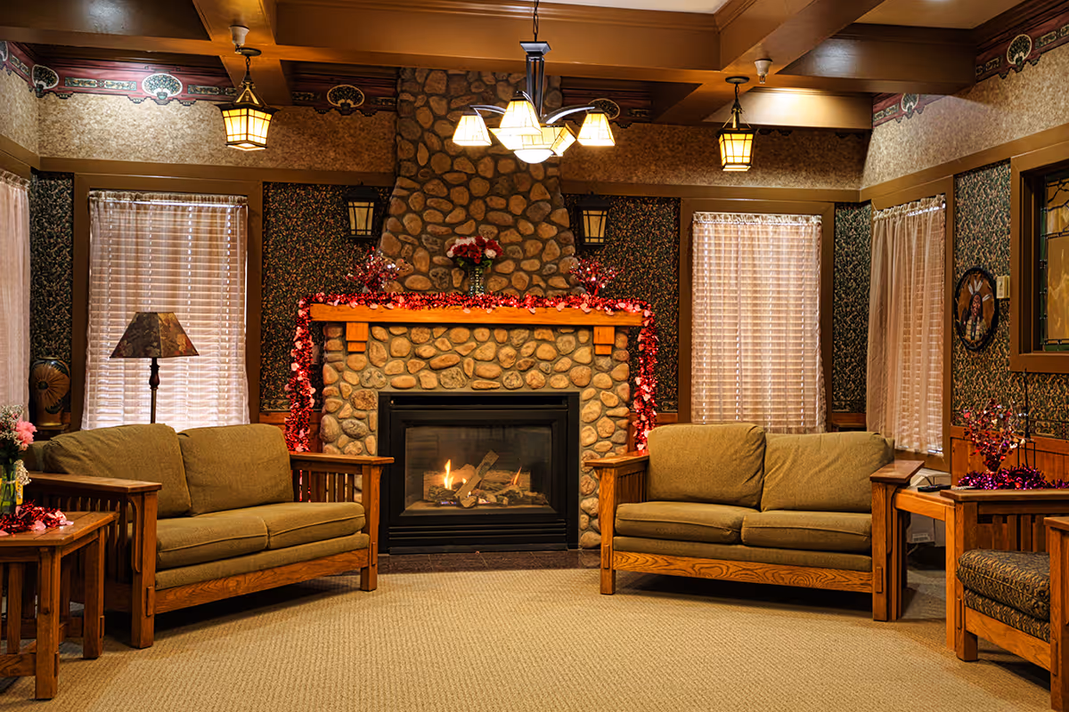 Cozy communal living room with a lit stone fireplace, two upholstered sofas, wooden side tables and warm lighting.