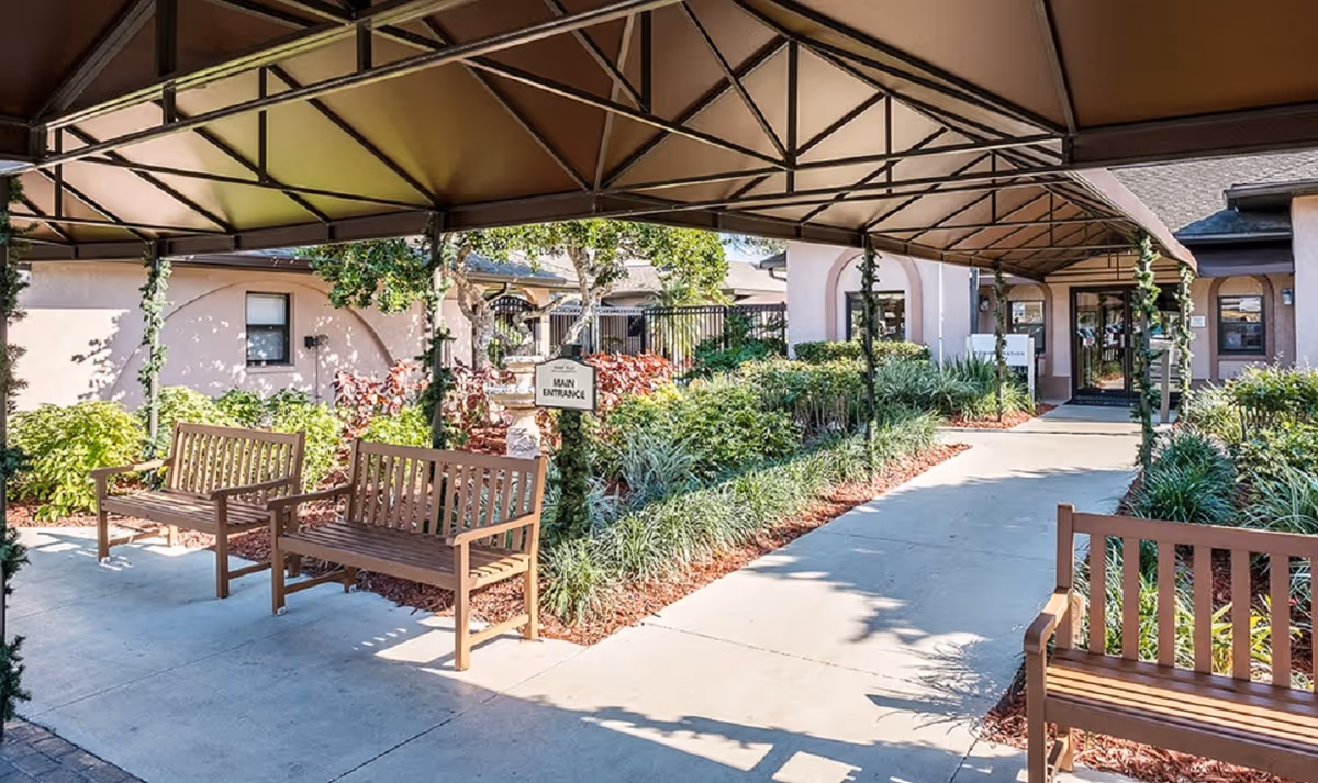 Covered entrance walkway with benches and landscaping leading to the main entrance of the facility.