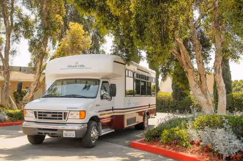 White shuttle bus parked in a landscaped driveway next to a senior living facility.