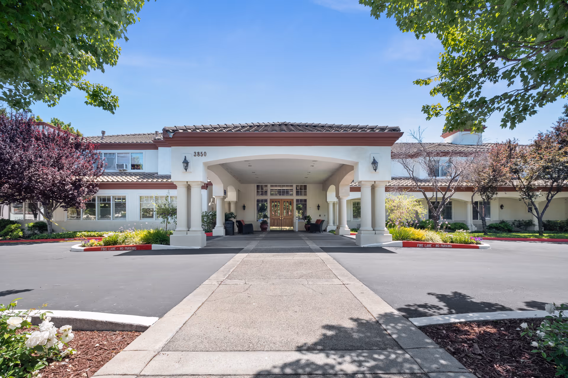 Covered entrance portico of a two-story residential care building with columns, double doors, a curved driveway and landscaped grounds.