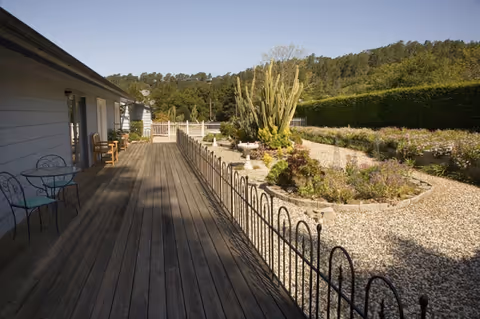 A wooden deck beside a building features metal chairs and a desert-style gravel garden.