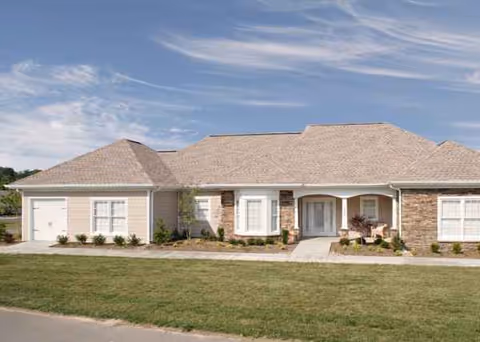 Single-story senior living building with tan brick, stone accents, front entrance, and manicured landscaping.