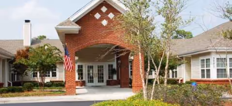 Front view of Brookdale Wilmington senior living building with brick archway, flag, and landscaping.