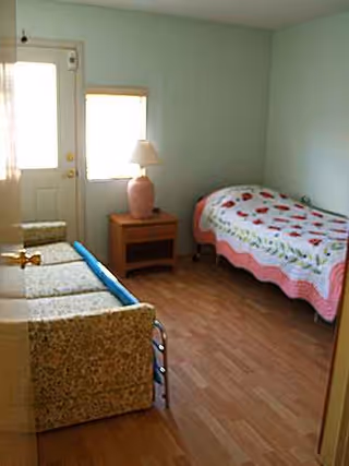 A small bedroom in a senior care home with a bed, sofa, and lamp.