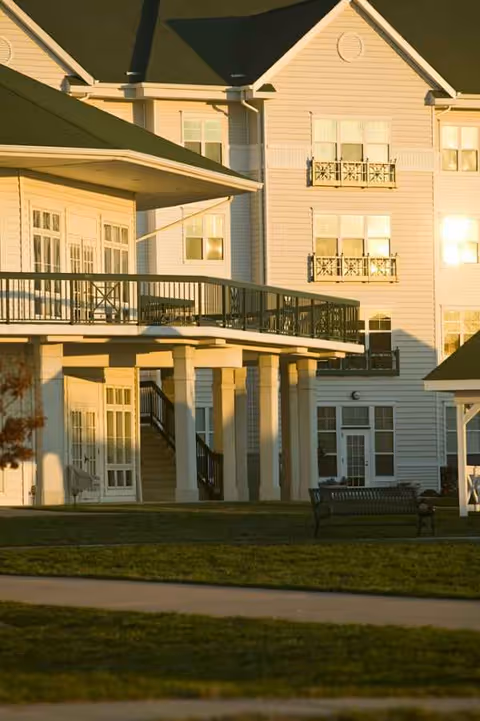 Exterior view of a multi-story senior living building with balconies and a bench.