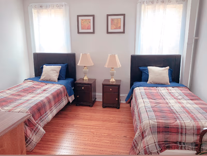Bright bedroom with two twin beds, two nightstands with lamps between them, and hardwood floors.