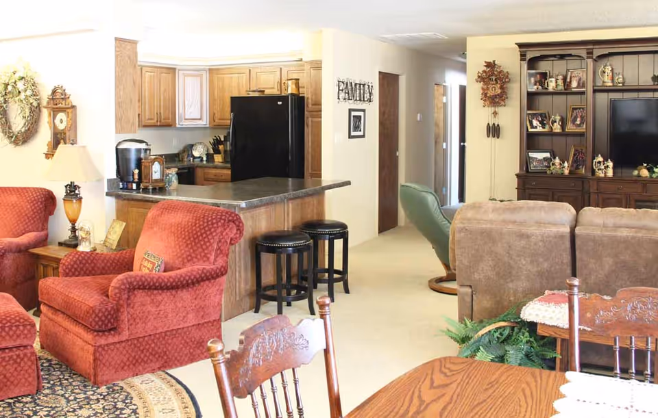 Open-plan living area with red upholstered armchairs, a kitchen island with stools, and a large entertainment cabinet with TV.