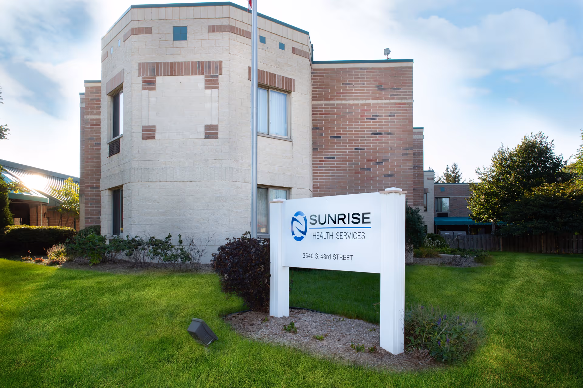 Front exterior of the Sunrise Health Services building with a white sign on a grassy lawn.