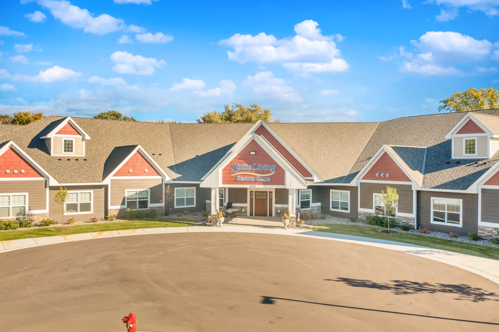 Front exterior view of Suite Living Senior Care of West St. Paul building with a circular driveway, clear blue sky, and some trees in the background.
