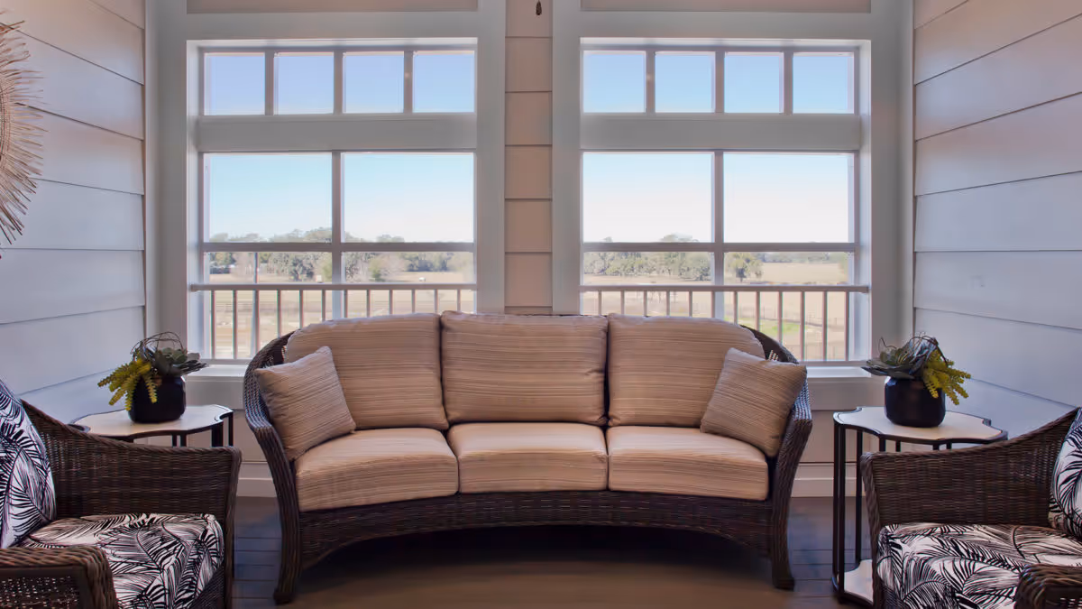 Wicker sofa and chairs arranged in a bright sunroom facing large windows with a countryside view.