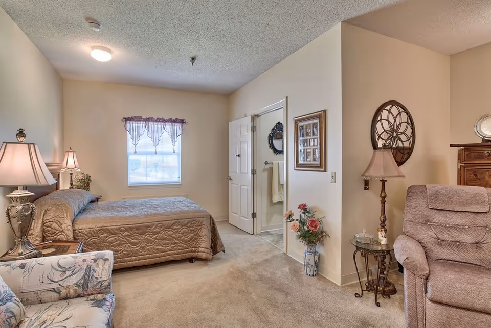 Furnished bedroom with a bed, bedside lamps, armchair, recliner, and a doorway to a bathroom.