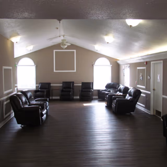 Large common room with a vaulted ceiling, wood floor, and leather recliners arranged along the walls beneath two arched windows.