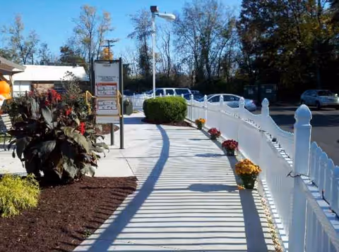 Outdoor walkway with white railing, potted flowers, and signage near a facility entrance.