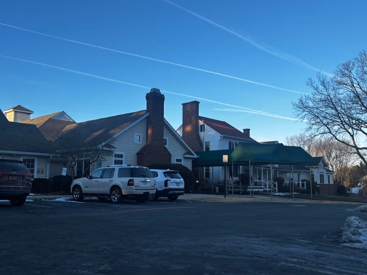 Front exterior of Meadow Glen of Leesburg building with a covered entrance, parked cars, and a clear blue sky.