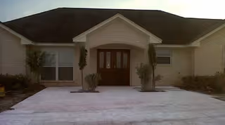Front exterior view of a single-story brick building with a dark roof, a central entrance with double wooden doors, and small shrubs planted near the entrance.