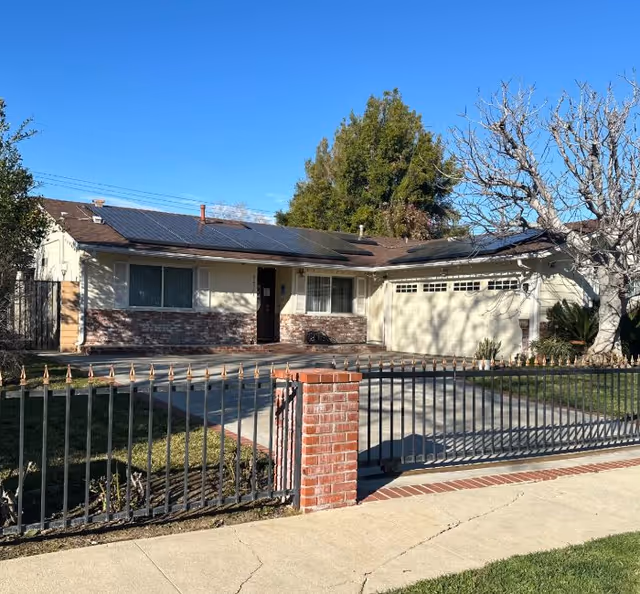 Single-story residential building with a gated front yard and solar panels on the roof.