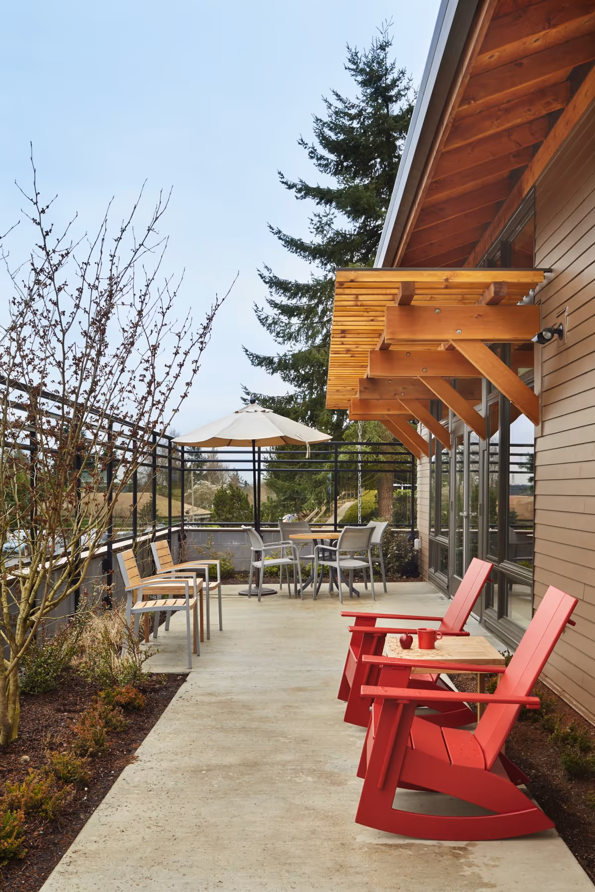 Outdoor patio beside a building featuring two red rocking chairs, a small table, additional seating and a patio umbrella.