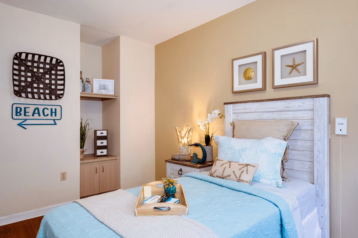Cozy beach-themed bedroom with a whitewashed headboard, light blue bedding, bedside table and coastal wall decor.
