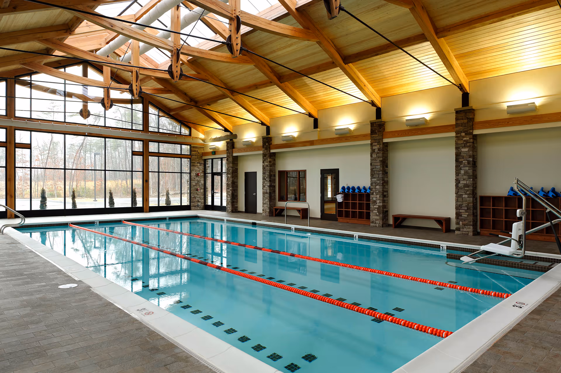 Indoor lap pool with red lane dividers beneath a wooden beamed ceiling and large windows.