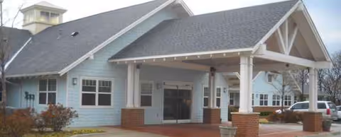 Blue, single-story senior living facility exterior with a covered front entrance and brick columns.