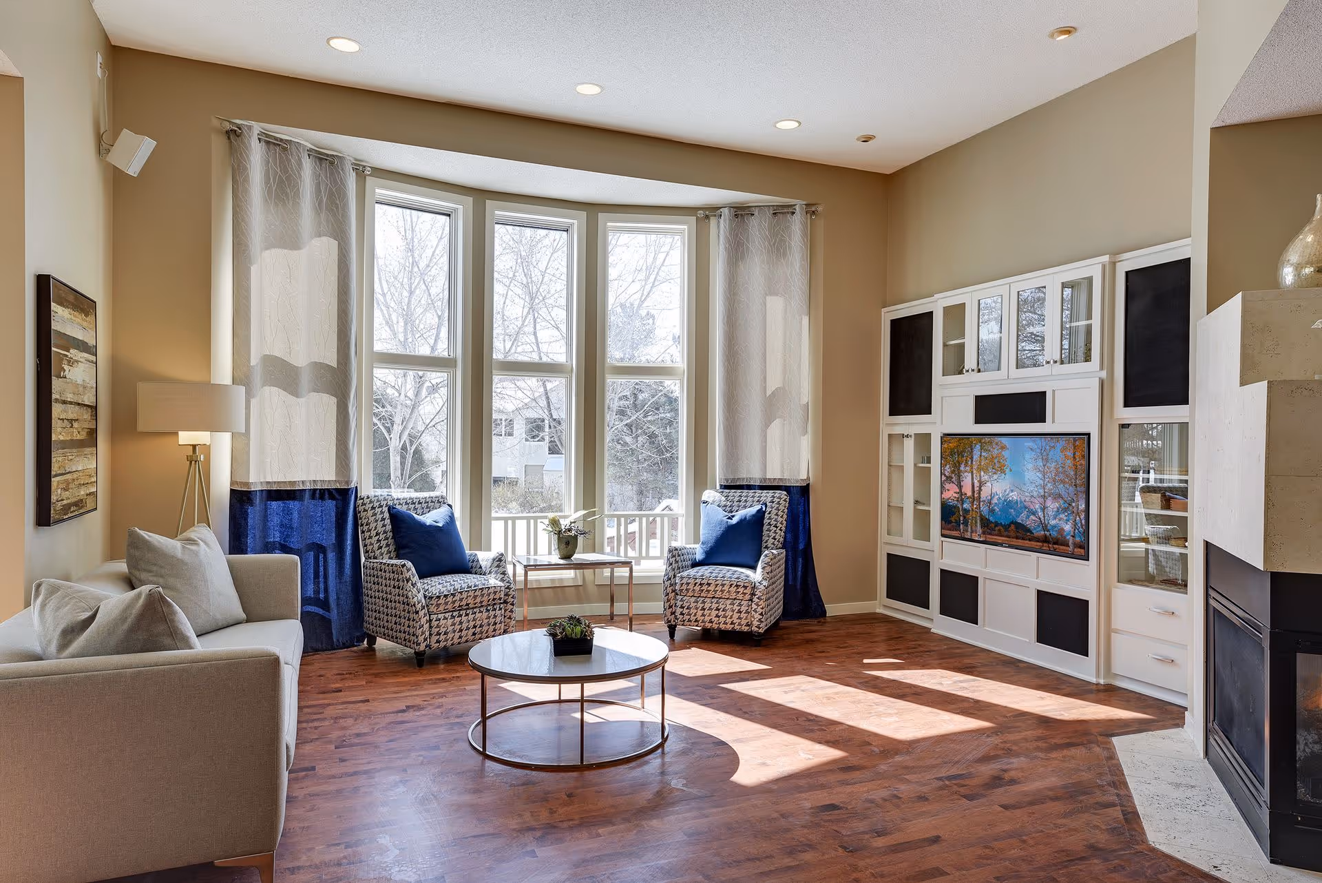 Bright living room with bay windows, a sofa and two armchairs around a round coffee table, built-in entertainment center and a fireplace.
