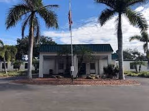 Front exterior of Woodbridge Care Center with palm trees and a flag out front.