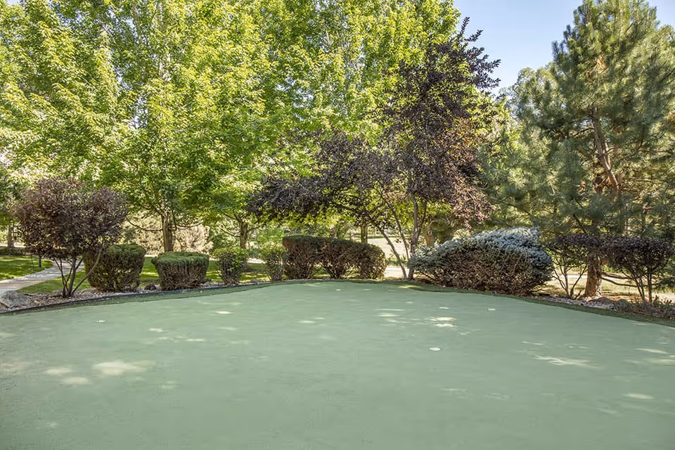 A small outdoor putting green surrounded by trimmed bushes and trees in a landscaped garden.