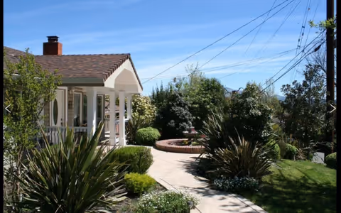 Exterior view of a house-style senior facility with a porch and manicured garden.