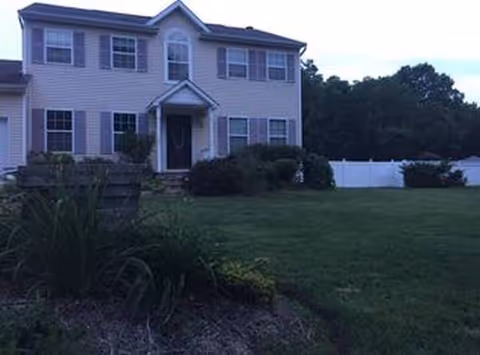 Two-story beige, house-style senior living facility with front yard and white fence.