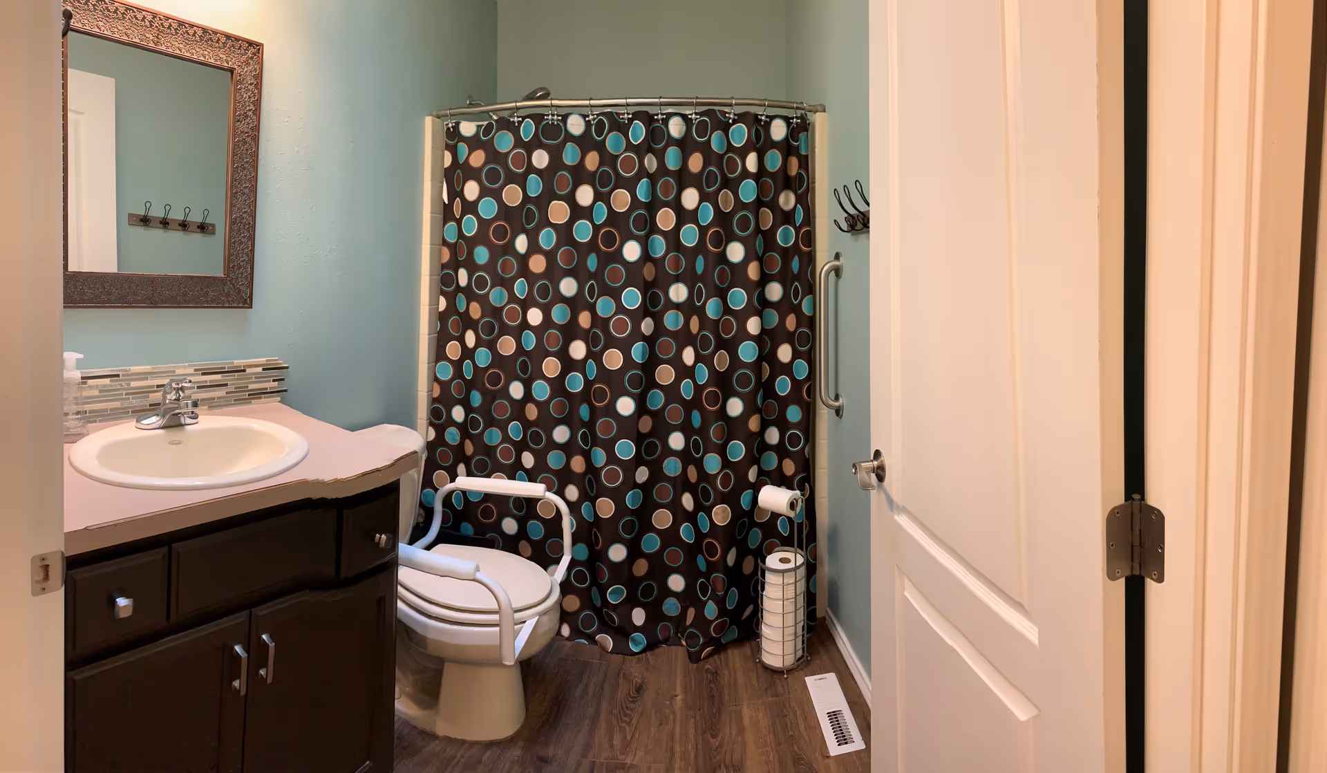 Bathroom with a sink and dark wood vanity, a toilet with white safety rails, and a polka-dot shower curtain.