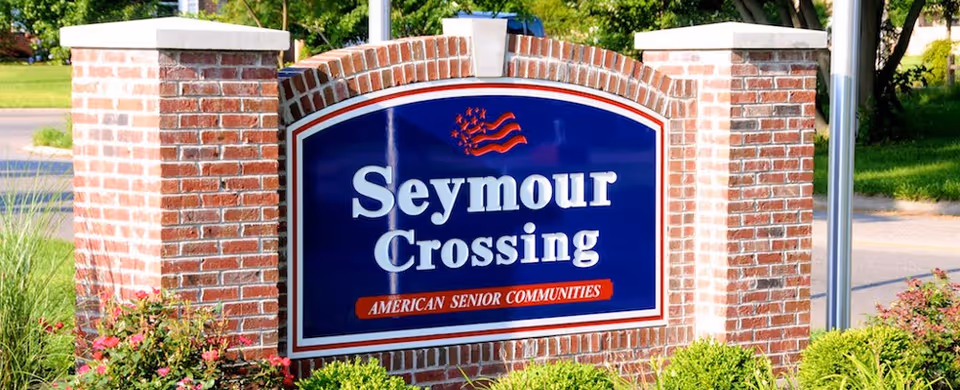 A brick sign for Seymour Crossing, an American senior community, set outdoors with greenery and a road in the background.
