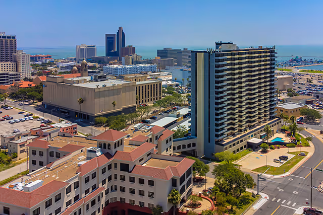 Aerial view of a coastal cityscape showing a tall multi-story residential tower near other buildings and the waterfront.