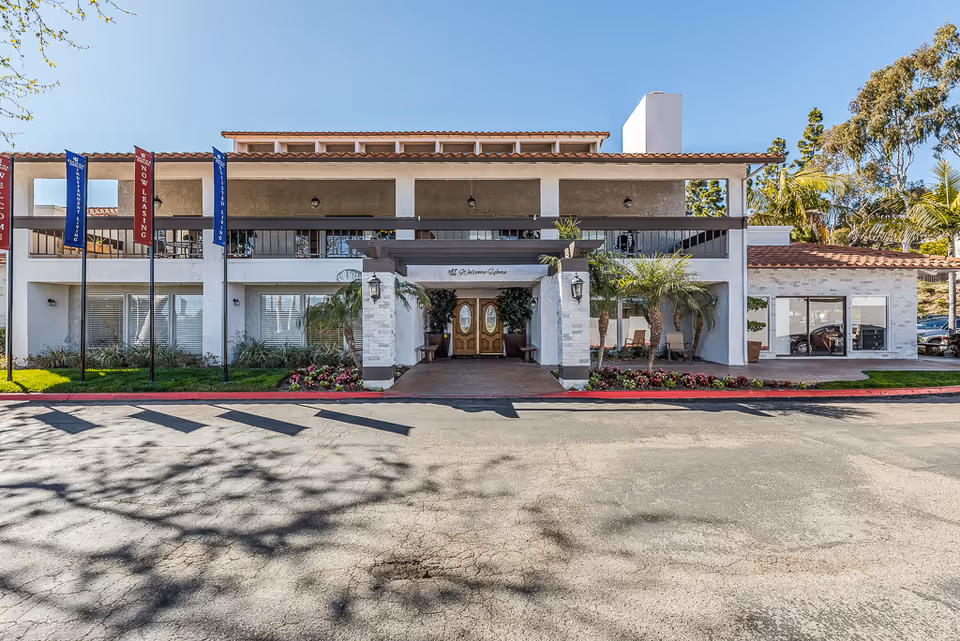 Front view of Encinitas Senior Living facility with flags, entrance, and landscaping.