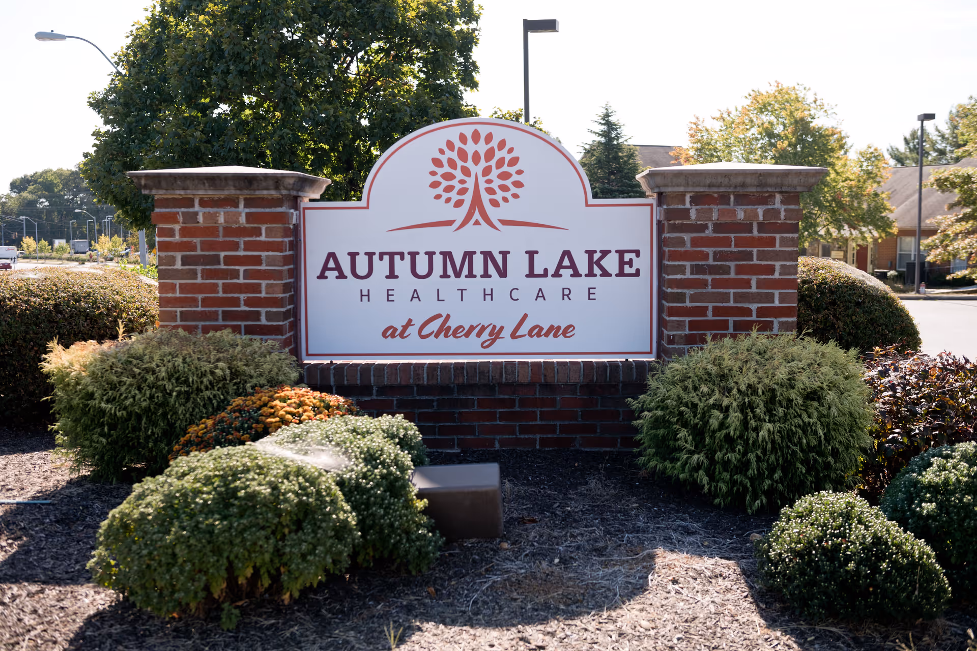 Entrance sign reading "Autumn Lake Healthcare at Cherry Lane" set between brick pillars with shrubs and landscaping in front.