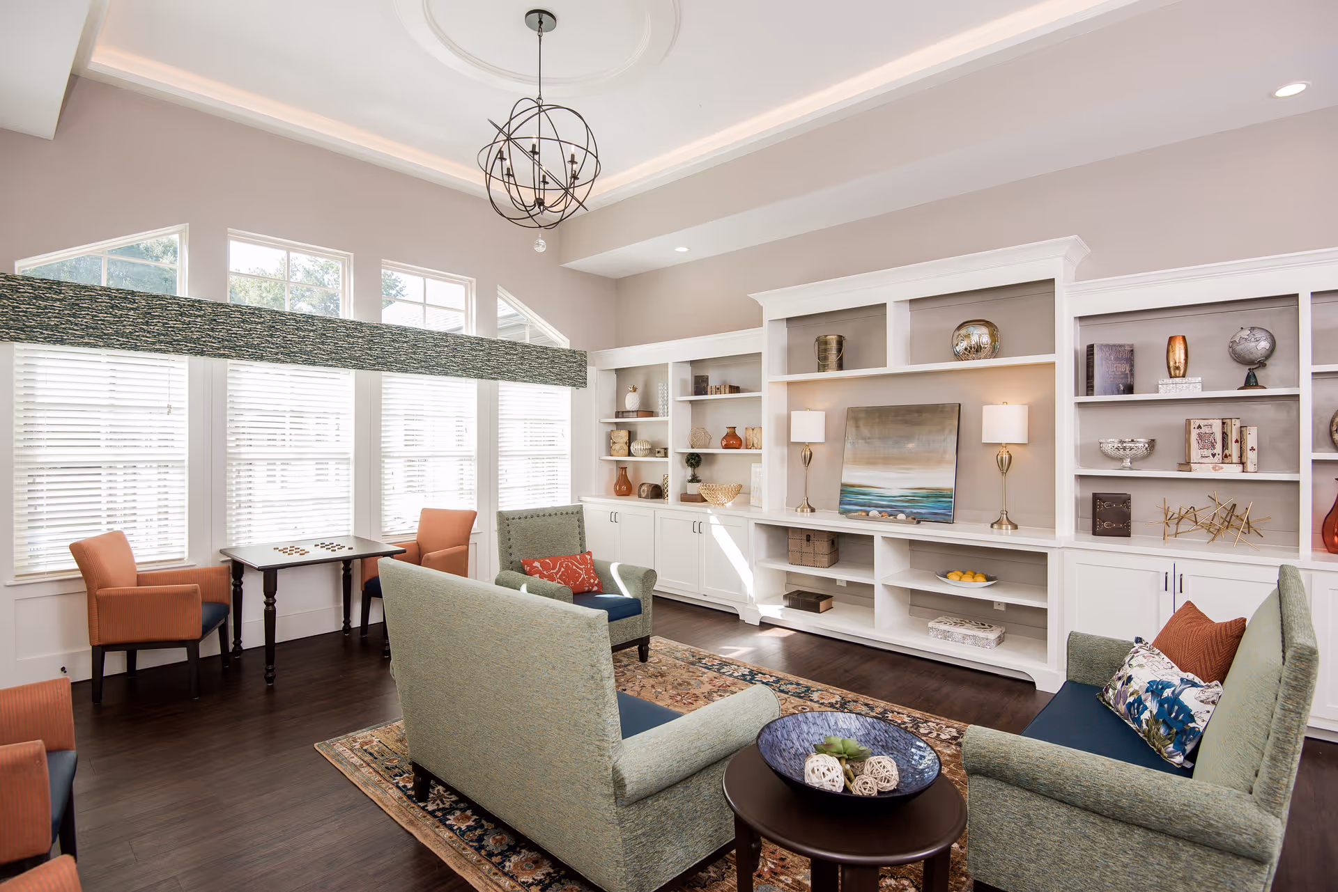 Bright communal living room with sofas, armchairs, a coffee table, built-in shelving and large windows.