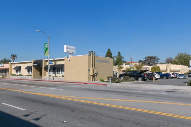 Exterior view of Shoreline Healthcare Center, a single-story beige brick building with a parking lot on the right side and a clear blue sky above.