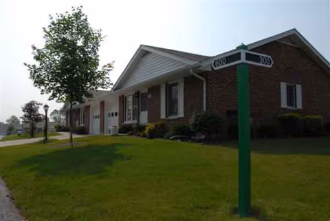 Brick senior living facility exterior with a green lawn, tree, and street sign.