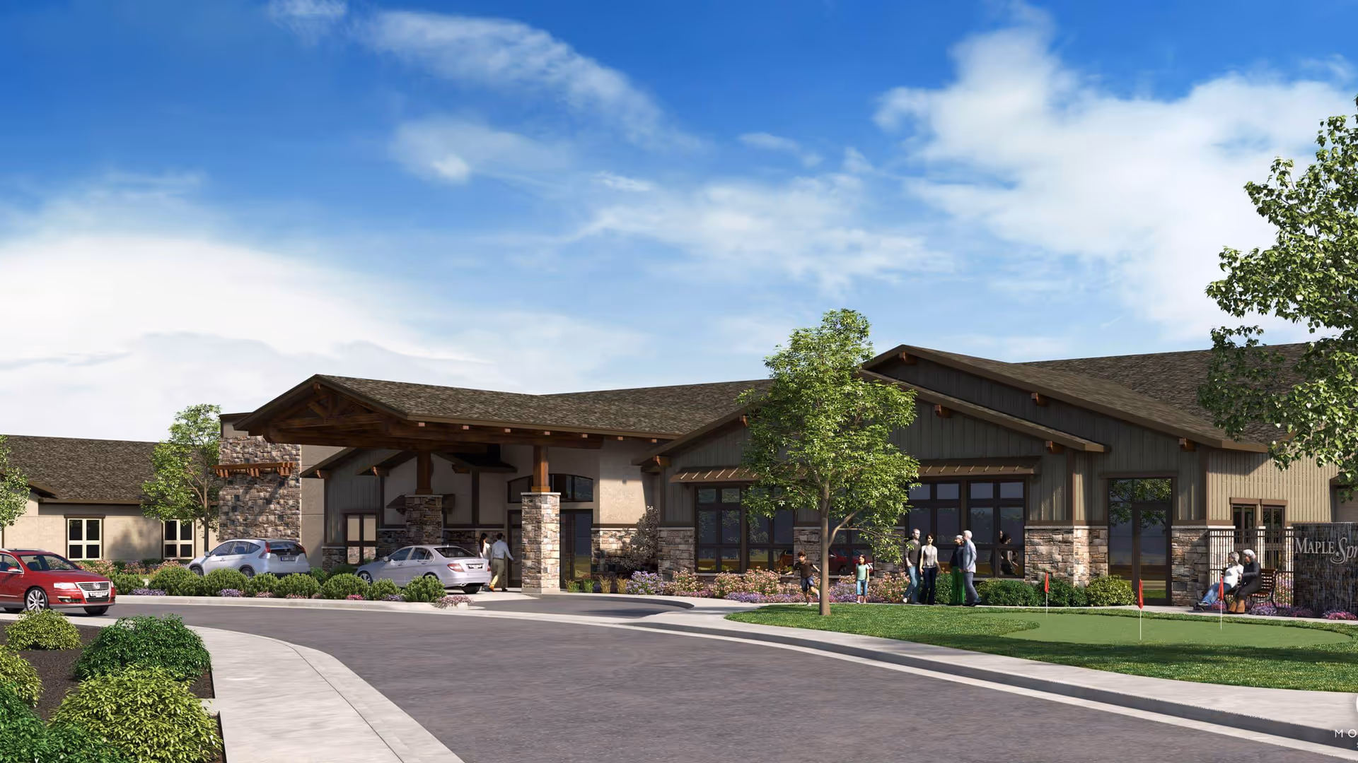 Exterior view of a single-story assisted living memory care facility with a covered entrance, stone and wood accents, landscaped greenery, and several people standing and sitting near the entrance. Cars are parked along the driveway under a partly cloudy sky.