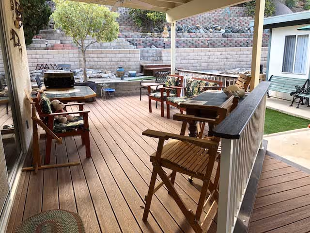 Covered outdoor wooden deck with chairs, tables, and potted plants overlooking a terraced backyard.