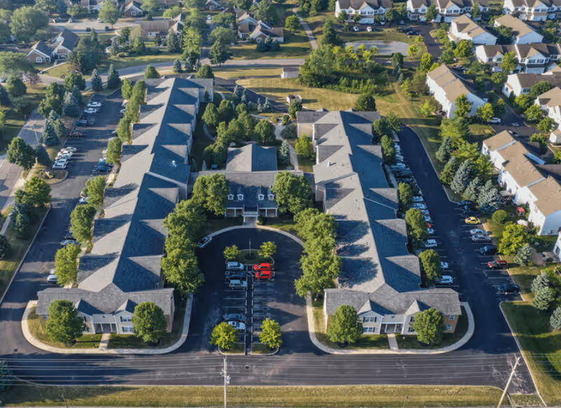 Aerial view of Wellington Village Senior Apartments with curved drive, parking, and trees.