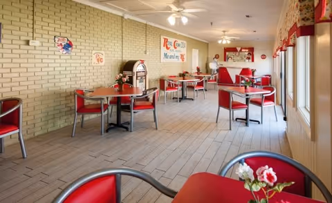 Bright retro dining room with red chairs and tables, a jukebox, and a small serving counter.