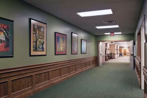 A long hallway in a senior living facility with framed artwork and green walls.