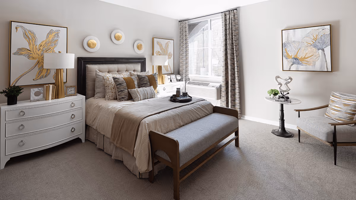 A bright, tastefully decorated bedroom with a large bed, nightstands, bench at the foot, an armchair and wall art.