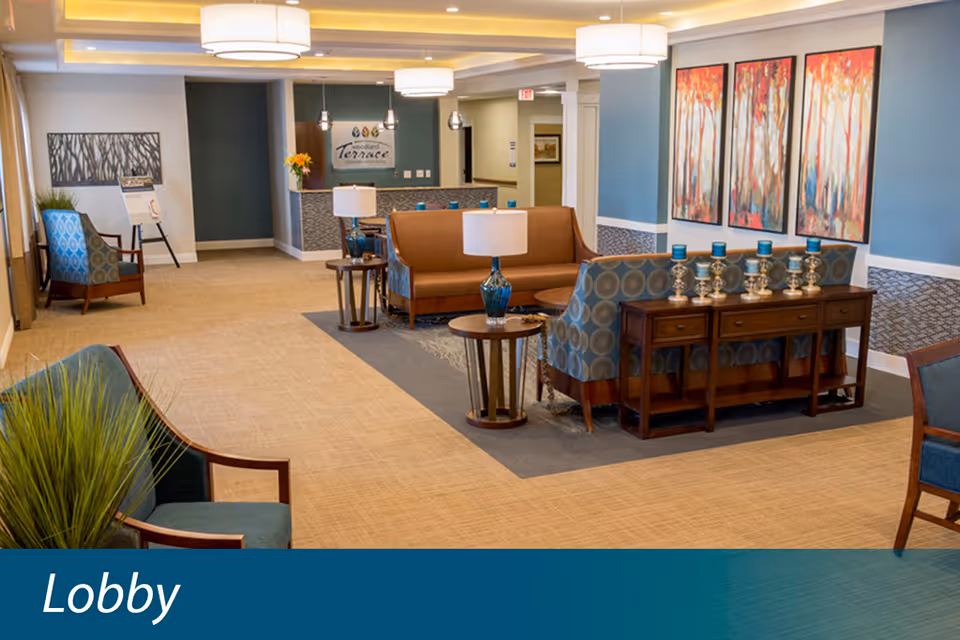 Furnished senior living lobby with seating areas, side tables, artwork, and a reception desk.