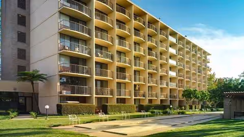 Front view of a multi-story senior living building with balconies and a manicured lawn.