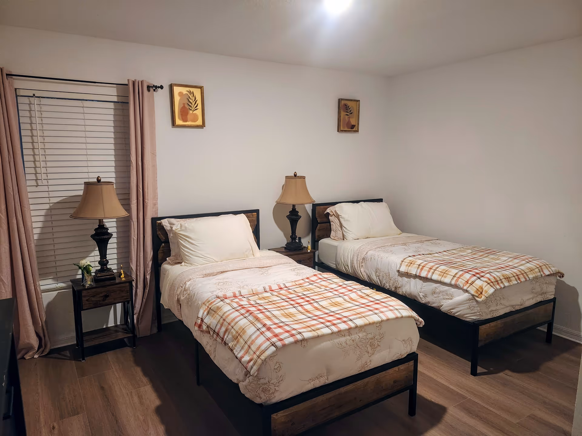 Two twin beds with plaid blankets, bedside tables and lamps in a simple, tidy bedroom.