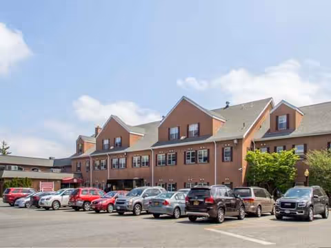 Brick senior living facility with a row of parked cars in the front parking lot