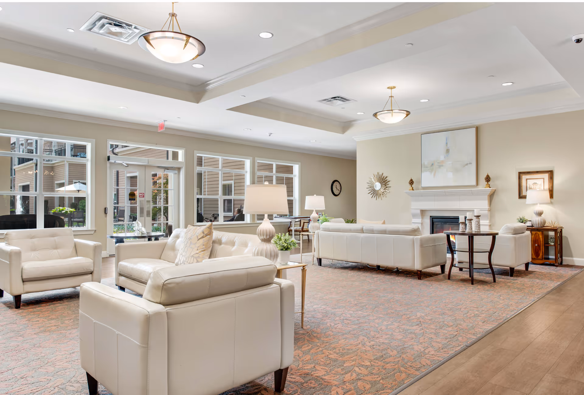 Bright, spacious lounge with cream sofas, tables, and a fireplace in a senior living facility.