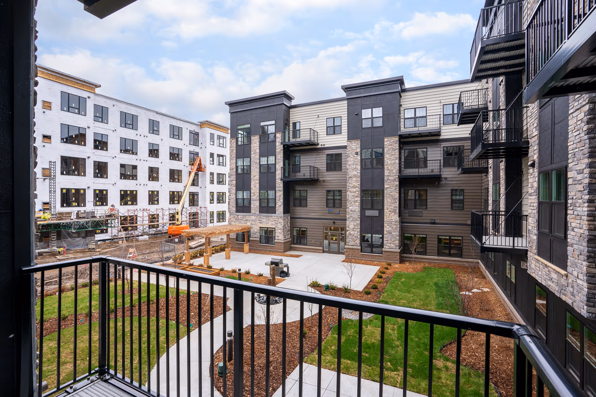 View from a balcony overlooking a landscaped central courtyard surrounded by multi-story apartment buildings, with construction on an adjacent building.